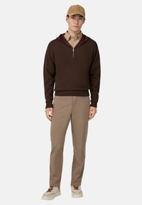 Hnedá mikina s krátkym zipsom a vínovým podšívaním, béžová košeľa s golierom, pieskové nohavice a krémové tenisky. Čiapka má tónové logo.