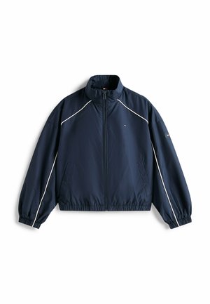 Chaqueta ligera azul marino con cremallera completa en el frente, ribetes blancos a lo largo de las mangas y los hombros, puños y dobladillo elásticos, y pequeño logo en el pecho y la manga.