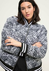 Prošívaná bomber bunda v černobílém květinovém vzoru, se žebrovanými černobílými manžetami, zapínáním na zip a volnějším střihem.