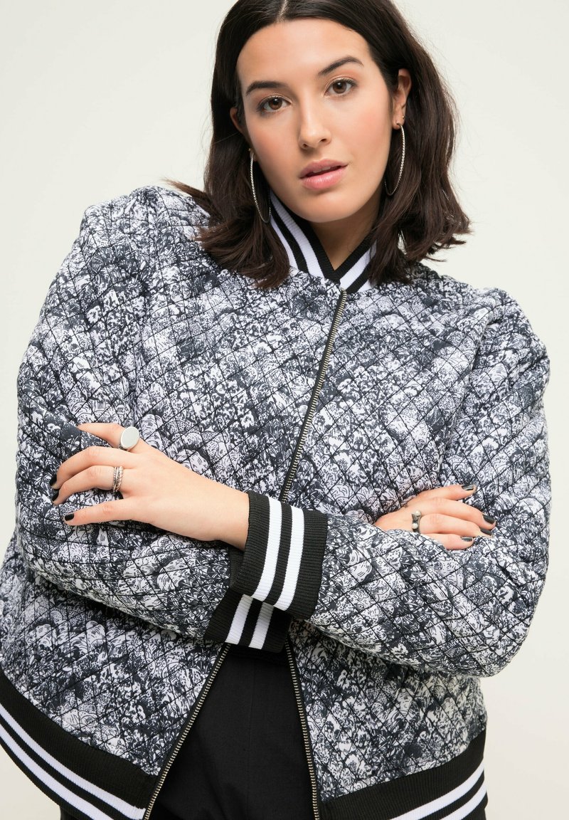 Prošívaná bomber bunda v černobílém květinovém vzoru, se žebrovanými černobílými manžetami, zapínáním na zip a volnějším střihem.