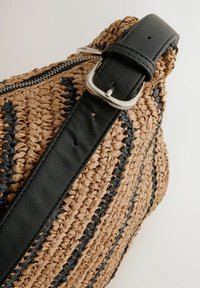 Vævet stråtaske i beige med sorte striber, har en sort læderrem og sølvspænde. Lynlåslukning synlig langs den øverste kant.