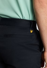 Sorte bukser med en baglomme, der har et gult broderet fuglelogo. Lavet af et glat stof med en ren, skræddersyet pasform.