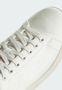 Hvide kanvas sneakers med tekstureret overdel, rund tå og flad snøre-design. Udgør metaløjer og en lysefarvet gummisål.