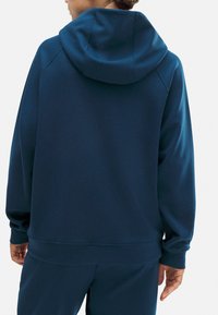 Sudadera azul marino hecha de una tela suave y texturizada, con una capucha grande, puños y dobladillo de canalé, con un corte holgado y sin logotipos visibles.