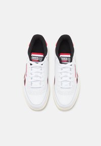 Hvide sneakers med en glat læderoverdel, røde detaljer og sort For. Snørebåndsdesign med perforeret tå for åndbarhed.