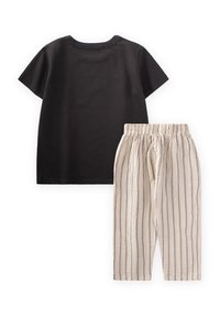Camiseta negra de algodón de manga corta combinada con pantalones crema con rayas verticales y una cinturilla elástica.
