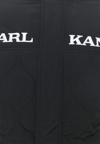 Giacca nera imbottita con texture trapuntata, logo "KARL" in bianco ben visibile e design semplice.