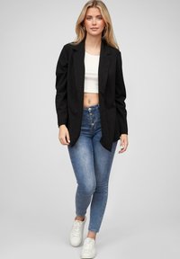 Fekete blézer, mely testre szabott fazonú, fehér, cropped felsővel és kék skinny farmerral párosítva. A ruhát fehér sportcipő egészíti ki.