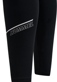 Zwarte leggings van zachte stof met een gladde textuur. Kenmerkt zich door een wit "HUMMEL" logo en een diagonale witte streepontwerp.