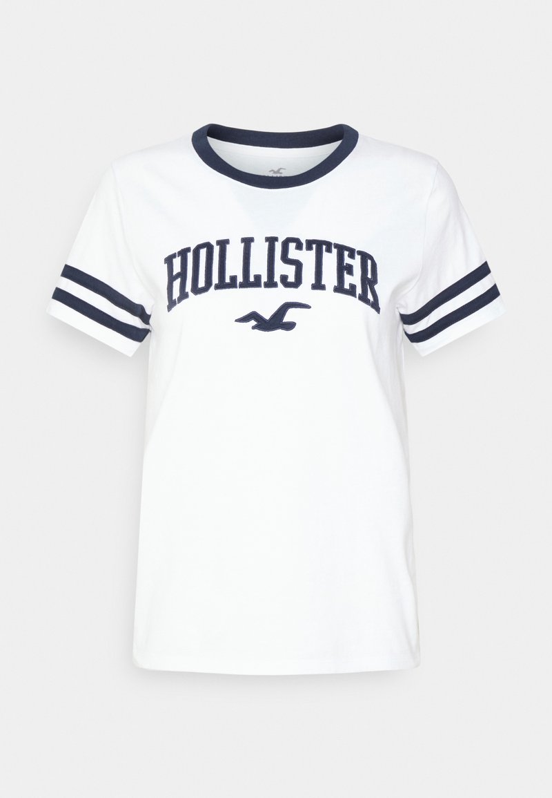 White t-shirt with navy blue collar and sleeve stripes. Features "HOLLISTER" in bold, navy font across the chest. Soft cotton material.