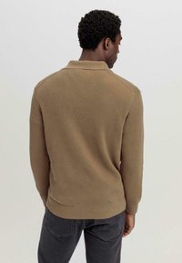 Brauner gerippter Strickpullover mit Polokragen und langen Ärmeln, der eine figurbetonte Silhouette und eine glatte Textur aufweist.