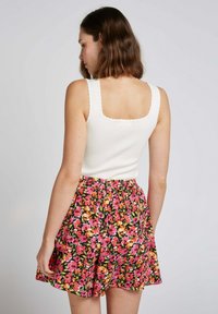 Haut blanc sans manches avec des bords festonnés associé à une jupe floral noire ornée de fleurs roses, oranges et jaunes. Taille élastique.
