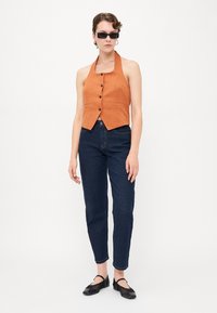 Oranžový lněný halter top s knoflíky ve spojení s tmavě modrými džínovými kalhotami tapered a černými plochými botami. Elegantní design s minimálními akcenty.