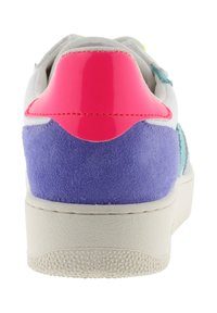 Sneaker bianco con suola testurizzata. Presenta un accento sul tallone lucido rosa e un pannello laterale in suede viola, con dettagli verdi vicino alla parte superiore.