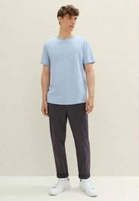 Light blue short-sleeve t-shirt with a round neckline, paired with dark gray trousers and white sneakers. Simple, casual design.