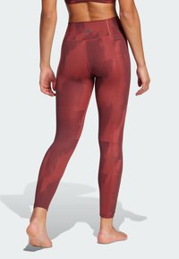 Højtaljede leggings i et bordeaux og rødt geometrisk mønster, med tekstureret materiale og et lille logo på taljen.
