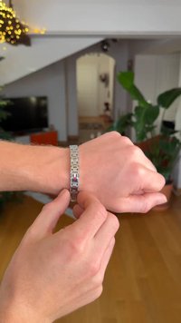 Silberne Metalluhr mit einem Gliederarmband, rechteckigem Zifferblatt und einem kleinen roten Akzent. Eine Hand verstellt den Verschluss an einem Handgelenk.