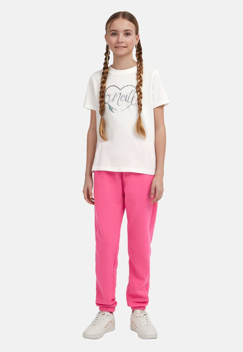 Bílý tričko s potiskem a tvarem srdce, v kombinaci s jasně růžovými tepláky se zakončením na elastické manžety a bílými teniskami.