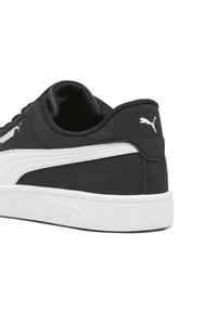 Čierne tenisky s hladkým syntetickým zvrškom, bielymi akcentmi a textúrovanou bielou gumovou podrážkou. Logo Puma zobrazené na boku a päte.