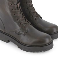 Botines de cuero marrón con suelas planas de goma, punteras redondas y ojales metálicos. Los cordones combinan con el color de la bota y cuentan con una marca sutil en el lateral.