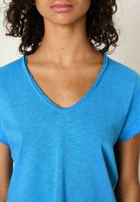 Modra V-majica s kratkimi rokavi, ki ima surove robove in mehko, strukturirano tkanino. Zasnovana za sproščen kroj.