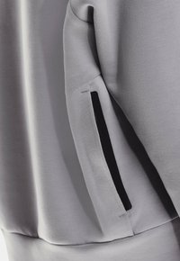 Tissu de sweat-shirt gris au toucher lisse ; il présente une poche zippée noire sur la manche gauche pour plus de fonctionnalité.