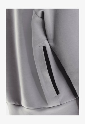 Grijze sweatshirtstof met een gladde textuur; heeft een zwarte zipzak op de linkermouw voor extra functionaliteit.