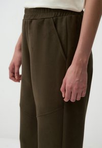 Olijfgroene broek met een relaxte pasvorm, gemaakt van zachte, textuurrijke stof, met een touwtje in de taille en zijzakken voor functionaliteit.