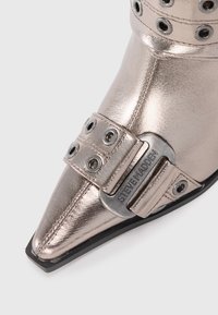 Botine metalice argintii cu vârf ascuțit, finisaj texturat, curea lată cu grommeturi circulare și detaliu cu cataramă branduită.
