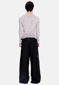 Pilkas ilgarankovis viršus su tekstūruotu paviršiumi, derinamas su juodomis plačiomis kelnėmis, kurios turi blizgių akcentų ir laisvą kirpimą.