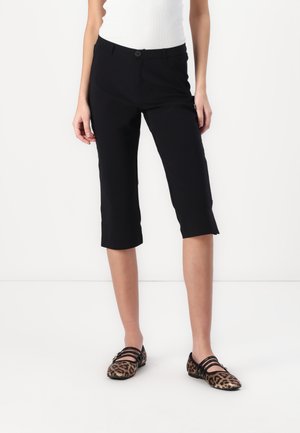 Black cropped trousers with a fitted design, featuring a single button closure and smooth texture, paired with leopard print flats.