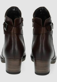 Botas de tobillo de cuero marrón con punta redonda, tacón apilado, detalle de hebilla y cremallera lateral. Textura suave y diseño sofisticado.