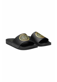 Black slides with a textured finish, wide straps featuring a gold lion emblem, flat sole, and minimalist design.