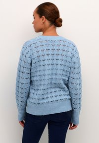 Hellblaue Strickjacke mit einem Spitzenmuster, gerippten Bündchen und Saum. Die Rückansicht zeigt ein Lochmuster und eine leicht übergroße Passform.