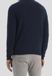 Marineblauwe gebreide trui met lange mouwen, ronde halslijn en geribde zoom, gecombineerd met lichtgrijze corduroy broek met zakdetails.