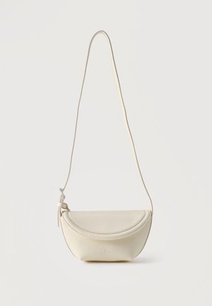 Petit sac bandoulière en cuir crème avec rabat incurvé et longue lanière fine suspendu sur un fond uni.