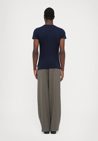 Marineblaues kurzärmeliges T-Shirt mit Rundhalsausschnitt, kombiniert mit weiten grauen Hosen, von hinten vor einem schlichten weißen Hintergrund gezeigt.