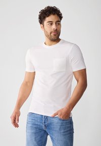 Hvit t-skjorte med korte ermer laget av teksturert stoff, rund hals og brystlomme, sammen med lyseblå denimbukser.