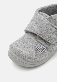 Sivi filcani slippers s čičak zatvaranjem, zaobljenim nožnim prstom i teksturiranim gornjim dijelom. Ima gumeni potplat i malu oznaku branda sa strane.