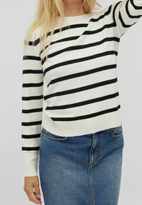Czarnobiały sweter w paski z okrągłym dekoltem, ściągaczami na mankietach i u dołu; w połączeniu z niebieską spódnicą jeansową o klasycznym kroju.