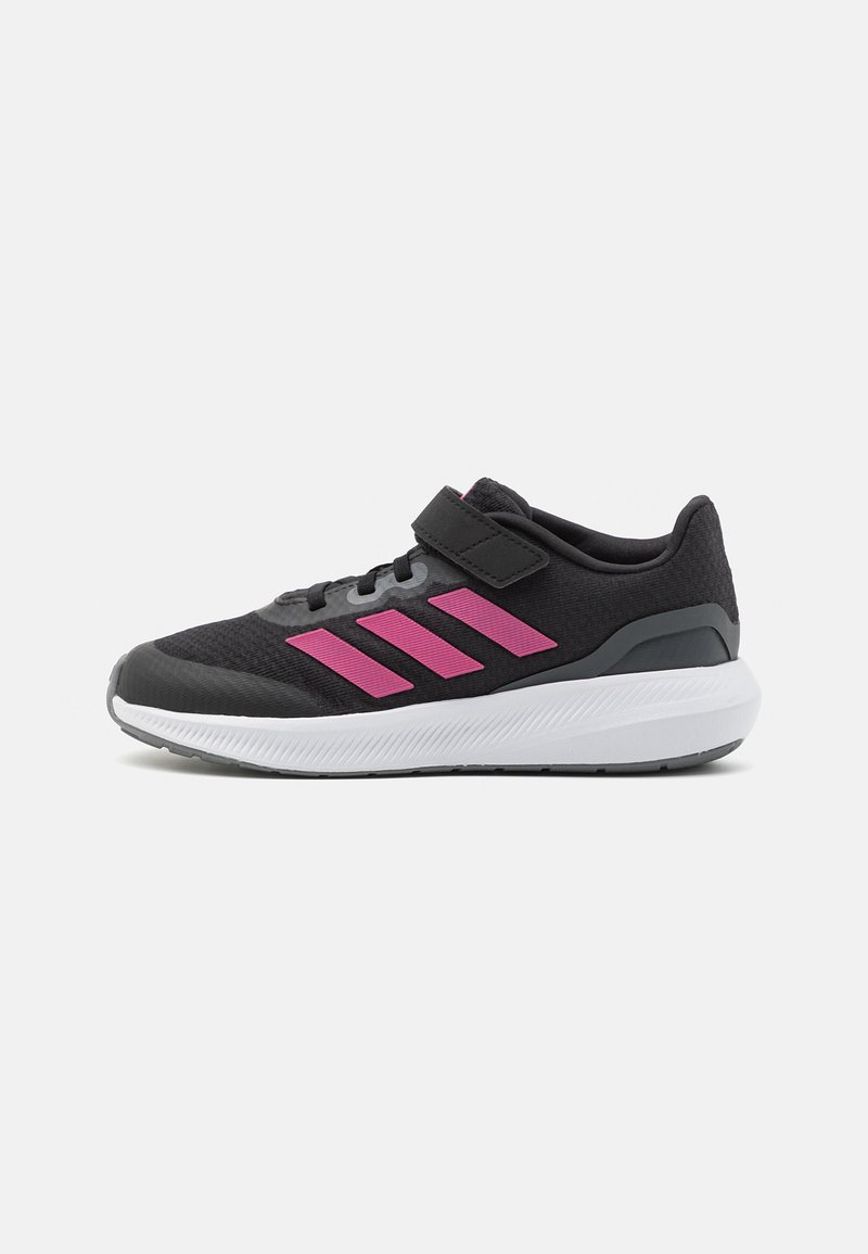 Zapatilla deportiva negra con parte superior de malla, detalles en rosa, tira de velcro y suela de goma blanca con un acabado texturizado.