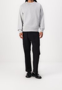 Šedá mikina s dlouhými rukávy a pružnými manžetami, v kombinaci s černými cargo kalhotami se bočními kapsami a uvolněným střihem, obuté s černými botami.