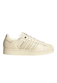 Λευκό παπούτσι Adidas Superstar με προστατευτική μύτη, τρεις ρίγες, κορδόνια και το κείμενο «Superstar» στο πλάι.