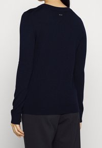 Pull en maille bleu marine avec un col rond, des manches longues et un détail discret du logo au dos. Texture douce et coupe ajustée.