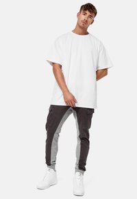 Witte oversized katoenen T-shirt gecombineerd met grijs en zwart tweekleurige joggers met zijzakken en geribbelde boorden. Schoenen zijn wit.