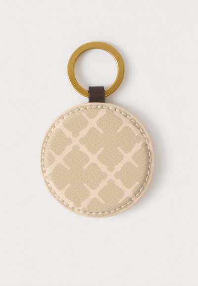Porte-clés rond en cuir beige avec un motif géométrique subtil et un anneau métallique doré attaché par une lanière en cuir marron foncé.