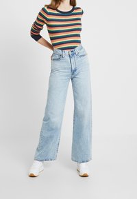 Raidallinen neulepaita punaisena, keltaisena, vihreänä ja laivastonsinisänä; korkeavyötäröiset vaaleansiniset leveälahkeiset farkut; valkoiset tennarit kumipohjilla ja yksityiskohdilla.