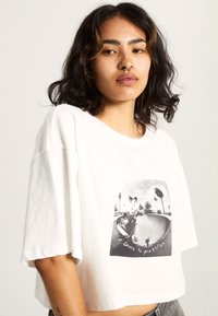 Witte cropped t-shirt van katoen, met een zwart-witte grafische print van een skateboarder met palmbomen en de tekst "SKATE TO YOUR RHYTHM".