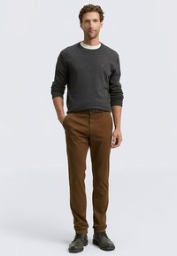 Donkergrijze trui, bruine broek en zwarte schoenen. De outfit heeft een ronde halslijn en een aansluitend ontwerp met een gladde textuur.