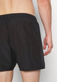Black swim shorts made of lightweight material, featuring an elastic waistband, a single back pocket, and a simple design.